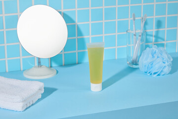 Round mirror and green-yellow cosmetic tube placed on a vibrant blue shelf. Cyan mosaic tile wall forms a modern, energetic background for wellness or cosmetic product visuals.