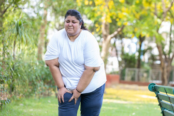 Fat indian woman suffering from knee pain while walking in summer park .overweight lady have joint...