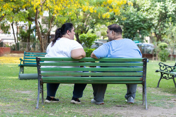 Happy Plus size indian couple sitting together at summer park. Overweight man and woman relaxing in...