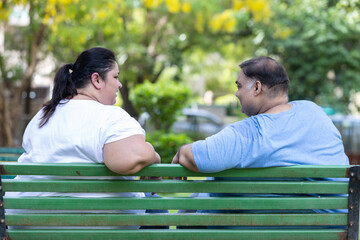 Happy Plus size indian couple sitting together at summer park. Overweight man and woman relaxing in...