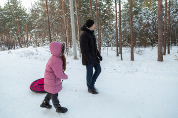 Dad with his daughter walking with snow tubing in the winter forest