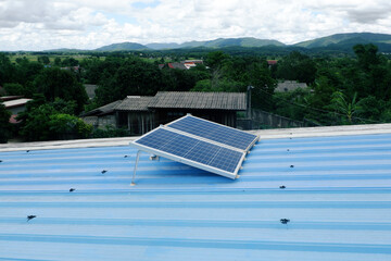 Two large solar panels are installed on a blue metal roof of a rural house using steel legs to support them.