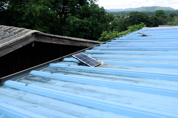 Small solar panels installed on the blue metal sheet roof of a rural house.