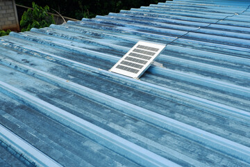 Small solar panels installed on the blue metal sheet roof of a rural house.