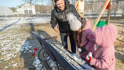 Grandfather with granddaughters making a little snowman in sunny winter day