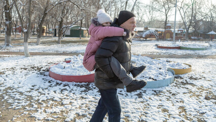 Grandfather playing with her granddaughter on the playground in the park in winter
