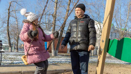 Grandfather playing with his granddaughter on the playground in the park in winter