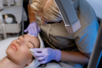 Esthetician cleansing woman's face with towel after facial treatment in beauty salon, young woman relaxing with closed eyes