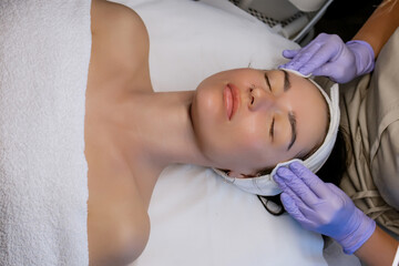 Esthetician cleansing woman's face with cotton pads after facial treatment in beauty salon