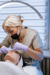Esthetician cleansing woman's face with towel after facial treatment in beauty salon, young woman relaxing with closed eyes