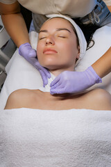 Esthetician cleansing woman's face with towel after facial treatment in beauty salon, young woman relaxing with closed eyes