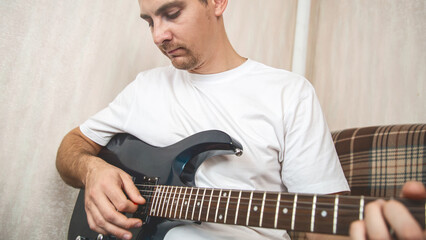 Musical hobby. Guitar skill. Man sitting on sofa playing string instrument enjoying learning chords...