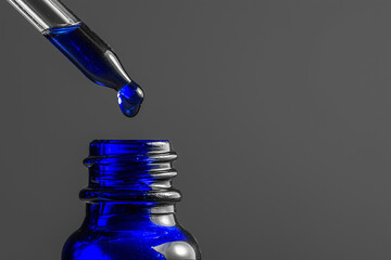  dropper dispensing blue liquid into bottle, concept of supplement or eye drop