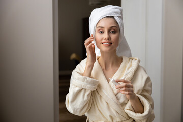 Woman with towel wrapped around her head gently applying cream into her skin