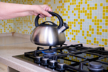 A woman's hand places a kettle of water on a gas stove. Home cooking