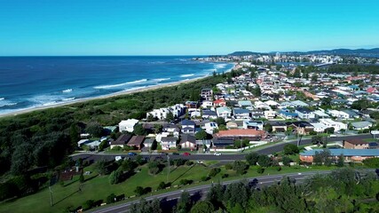 Drone aerial landscape of urban town suburbs with ocean waves crashing on shoreline and housing homes on street with road highway North Entrance Central Coast Australia community urban infrastructure