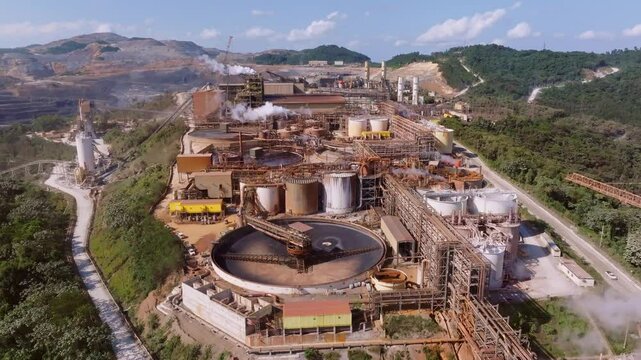 Barrick Gold mine complex showing large scale concentrators, tanks, pipes, steam vents, and surrounding hills in Cotu&iacute; Republic. Aerial flyover