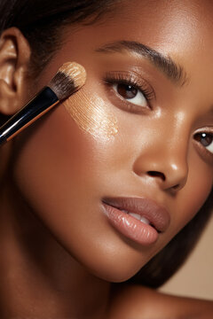 Flawless dark skin woman applying foundation with brush, showing smooth glowing complexion and natural beauty