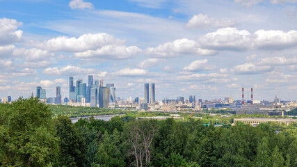 Breathtaking view of Moscow skyline from Vorobyovy Gory, with Moscow River, green trees, and clouds in the blue sky. The Moscow skyline dominates the horizon, creating a stunning scene