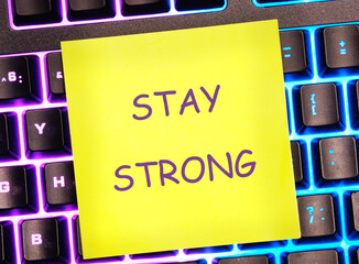 STAY STRONG message written on a bright yellow sticker on a colorful keyboard