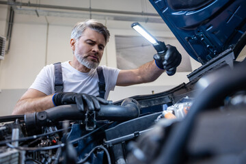 Mechanic using flashlight on engine