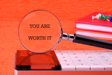 YOU ARE WORTH IT words focused through a magnifying glass on an orange background, based on a...