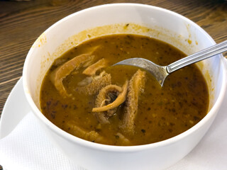 Bowl of Slovak tripe soup with spoon. Traditional beef tripe in red paprika broth. Close-up view of hot soup in white bowl.