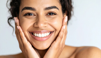 Radiant woman smiles, cradling her face with her hands. Her perfect teeth and clear skin shine with beauty and confidence.