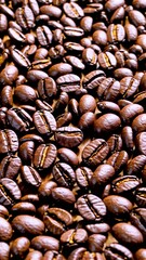 Roasted coffee beans scattered across rustic wooden surface, forming rich, intricate pattern with deep brown tones and varied textures