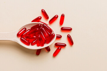 Vitamin capsules in a spoon on a colored background. Pills served as a healthy meal. Red soft gel vitamin supplement capsules on spoon