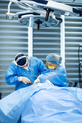 Surgeons in complex operation. Two surgeons in blue scrubs conduct an intricate surgery, focused on...