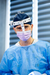 Surgeon smiling in operating room attire. A surgeon wearing a blue gown and mask smiles confidently...