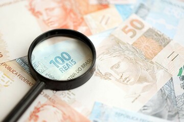 Brazilian reais banknotes and magnifying glass. The current Brazil real money bills and loupe