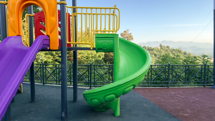 colorful playground slide set against a backdrop of lush green hills and a clear blue sky, offering a fun spot for children with a scenic view