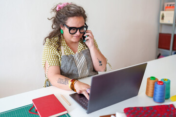 Skilled seamstress working in studio, processing client orders on laptop while engaging in phone conversation