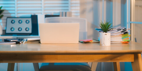 A well-lit, modern office space features a wooden desk with a laptop, tablet, and plant, suggesting...