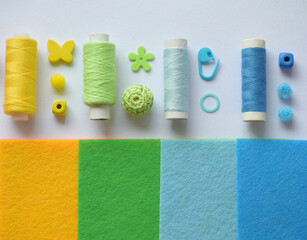 felt rectangles in yellow, green, blue serve as background for neatly placed thread spools, yarn...