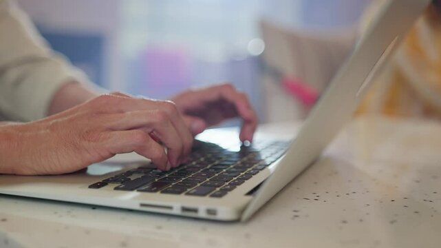 The hands of an old man typing anxiously on a laptop keyboard, pressing the delete or backspace button multiple times, sitting in a coffee shop or cafe. Concept of technology and senior citizens. 
