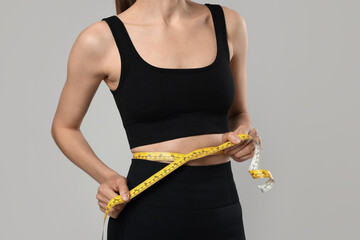 Woman measuring her belly with tape on gray background, closeup