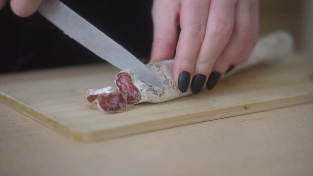 Slicing fuet salami into thin slices using a knife. Preparing a delicacy at home. Closeup shot