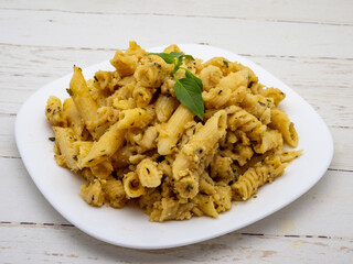 mix of penne quatro formaggi garnished with basil leaf on top on white plate