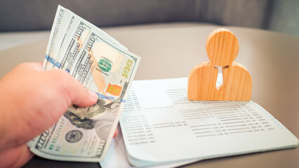 Obraz premium Boss counting dollars to pay employees' accounts in company with wooden employee model and blurred image of bankbook