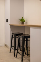 Kitchen bar area with wooden counter, two black bar stools and small potted plant on the surface