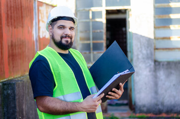 Portrait of male factory or industry worker wearing safety gear holding a folder or a binder...