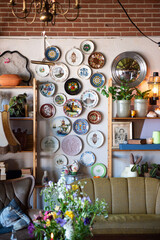 Vertical image of the interior of an old house with a sitting area decorated with vintage furniture and antique colored ceramic plates on the wall with plants and wild flowers in a vase.