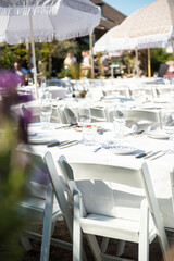 Vertical image of wedding vibes with white-covered tables, parasols, and folding chairs set up outdoors on a sunny summer day during a wedding in the Netherlands.