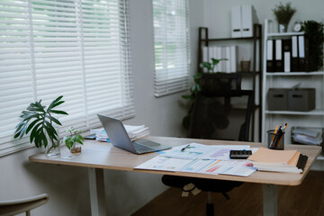A laptop and graphs sit on a conference table in a brightly colored, empty conference room.