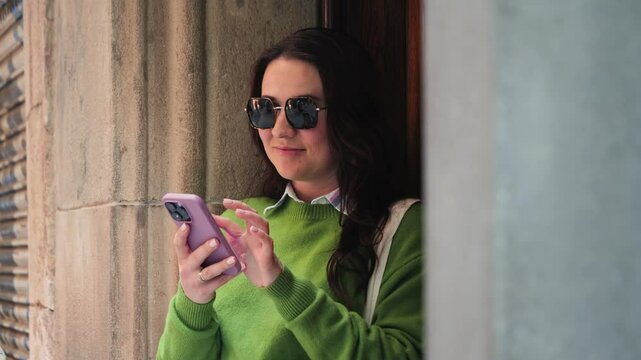 Smiling woman using smartphone on street in europe city. Person chatting with friends, using chat ai, social media. High quality 4k footage
