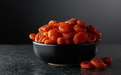 Organic dried apricots in a black dish against a black background.