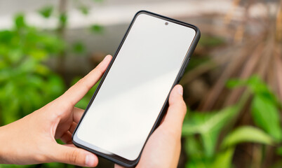 Hand holding smartphone with blank screen for graphic display montage on outdoors background, mockup display for lifestyle and wireless technology.